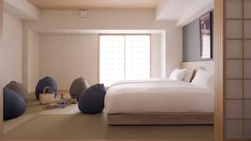 Une chambre à coucher au style minimaliste, avec un grand lit, un futon et un fauteuil-futon. Une fenêtre offre une vue sur l’extérieur.