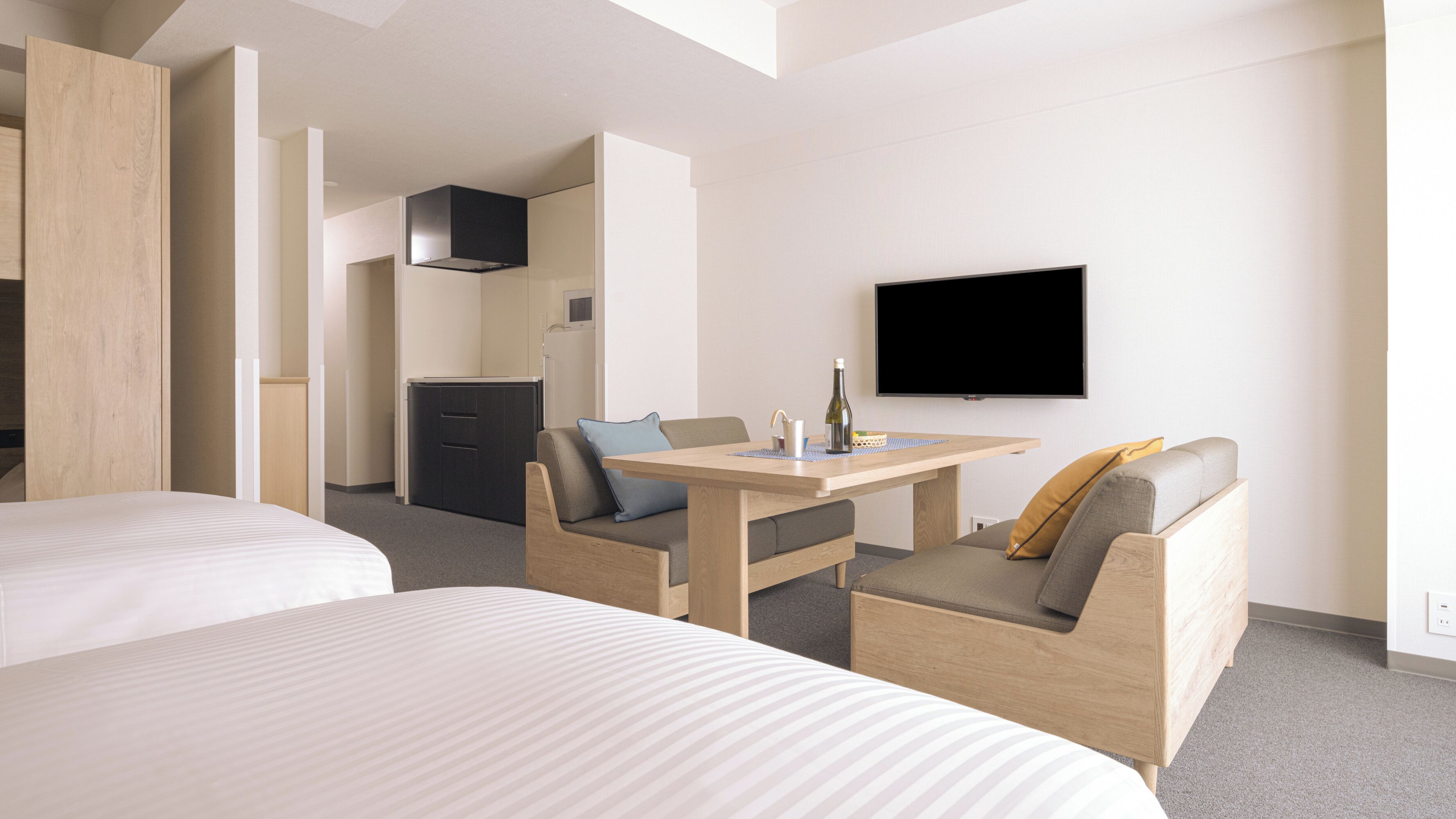 Una habitación de hotel con dos camas, una mesa de comedor, un televisor y un kitchenette.