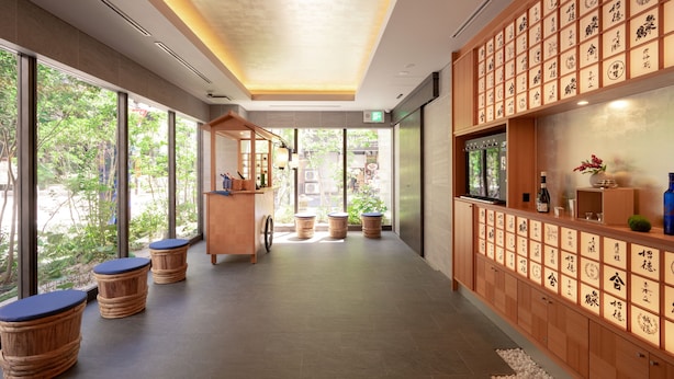 A modern interior with a wooden reception desk, large windows, and a wall with calligraphy. - MIMARU Osaka Shinsaibashi East (Osaka)