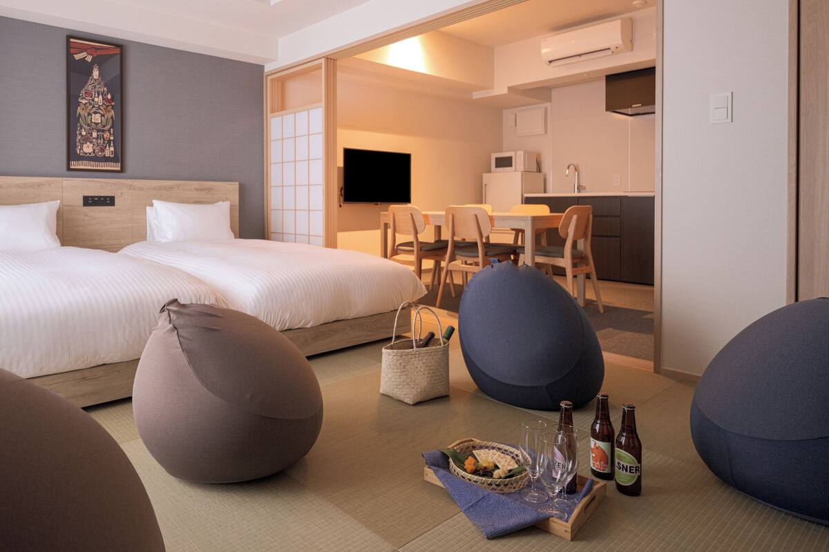 A hotel room with two beds, a dining area, and a kitchenette.