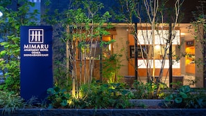 The exterior of the Mimaru Apartment Hotel in Shinsaibashi East, featuring a well-lit entrance, lush greenery, and a modern building facade. - MIMARU Osaka Shinsaibashi East (Osaka)