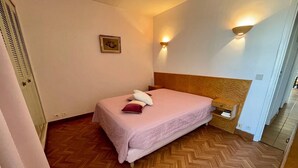 A bedroom with a bed, a nightstand, a wall-mounted light, a picture on the wall, and a wooden floor. - Seafront apartment with private parking (La Ciotat)