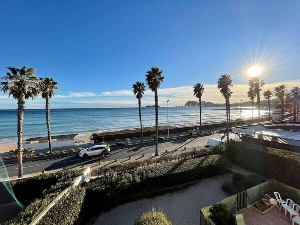 A coastal road with palm trees, a beach, and a clear sky.