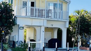 Una casa de dos pisos con un balcón, un garaje y un muelle que se extiende sobre el agua.