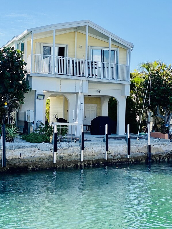 A two-story house with a balcony, a garage, and a dock extending into the water. - Open Water View from porch , golf cart, dock, bikes, kayaks, trailer parking (Cudjoe Key)