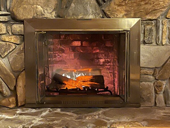 A stone fireplace with a metal frame, burning logs. - Romantic,Cozy Log Cabin, Hot Tub, WiFi, pool table (topton)