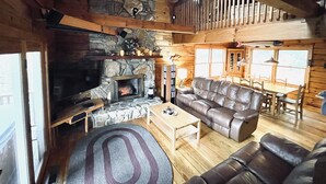 Ein gemütliches Blockhaushaus-Interieur mit Kamin aus Stein, Ledersofas, Holzböden und einem Essbereich.