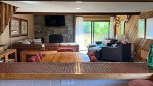 Un espacio habitable amplio con techo de madera, chimenea de piedra, un sofá grande y un televisor montado en la pared.