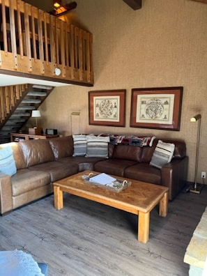 A living room with a brown leather sectional sofa, a wooden coffee table, and two framed pictures on the wall.