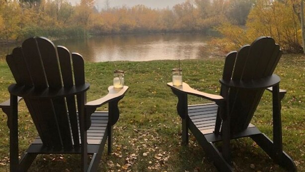 Dos sillas Adirondack mirando a un lago con montañas brumosas al fondo.