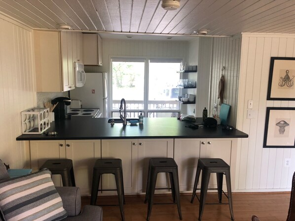 A kitchen with white cabinets, a black countertop, and a window. There are three stools and a chair.