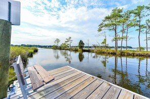 A wooden dock extending into calm water with trees and a clear sky in the background.