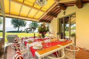 Un espace de restauration extérieur abrité, avec une table dressée pour un repas, des chaises et une vue sur le paysage.