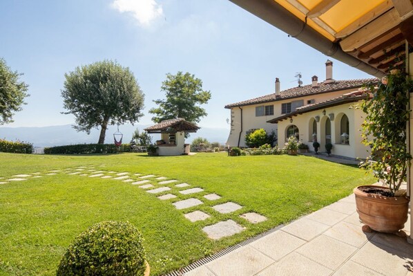 A well-maintained lawn with stepping stones, a potted plant, and a building with arches and a tiled roof.