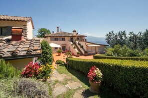 A villa with a terracotta roof, a stone pathway, and a view of the mountains.