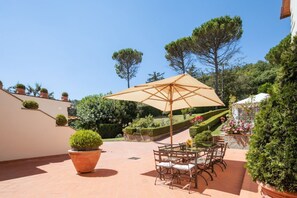 A patio with a table and chairs, a large umbrella, and potted plants.
