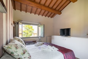 A bedroom with a bed, a window, a mirror, a television, and a wooden ceiling. - Villa Collesole by MMega (Rignano sull'Arno)