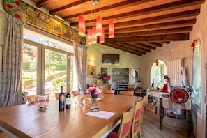 A rustic interior with a wooden ceiling, a dining area with a table set for two, and a kitchen area with a red appliance. - Villa Collesole by MMega (Rignano sull'Arno)