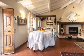 A dining area with a round table, chairs, a fruit bowl, a fireplace, and a mirror.