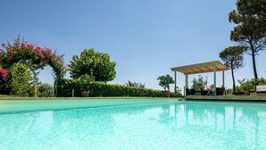 Una piscina cristalina con una pérgola y zona de estar, rodeada de exuberante vegetación y árboles.