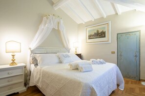 A bedroom with a canopy bed, bedside lamps, a nightstand, a door with decorative trim, and a framed picture on the wall.
