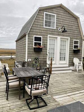 A wooden deck with a table and chairs, a small shed with windows and a door, and a view of the landscape.