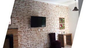 Un salon avec un mur en briques, un téléviseur à écran plat fixé au-dessus, un canapé de couleur foncée et une petite table en bois.