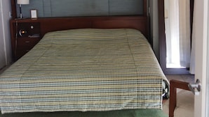 Een slaapkamer met een geruit beddegoed, een houten hoofdbord, een nachtkastje met een lamp en een groen vloerkleed.