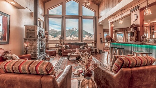 A spacious living room with leather sofas, a fireplace, and a large window offering a mountain view. - Cutbow Bend (Livingston)