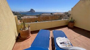 Un balcone con due poltrone blu, una pianta in vaso e vista sul mare e sulla città.
