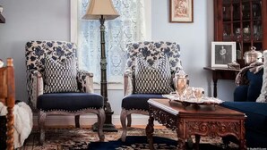 Un salón tradicional con dos sillones estampados, una lámpara de pie, una mesita auxiliar con bandeja y un sofá azul.
