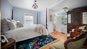 Un dormitorio con una cama con dosel, un candelabro, un tapete floral y un aparador de madera.