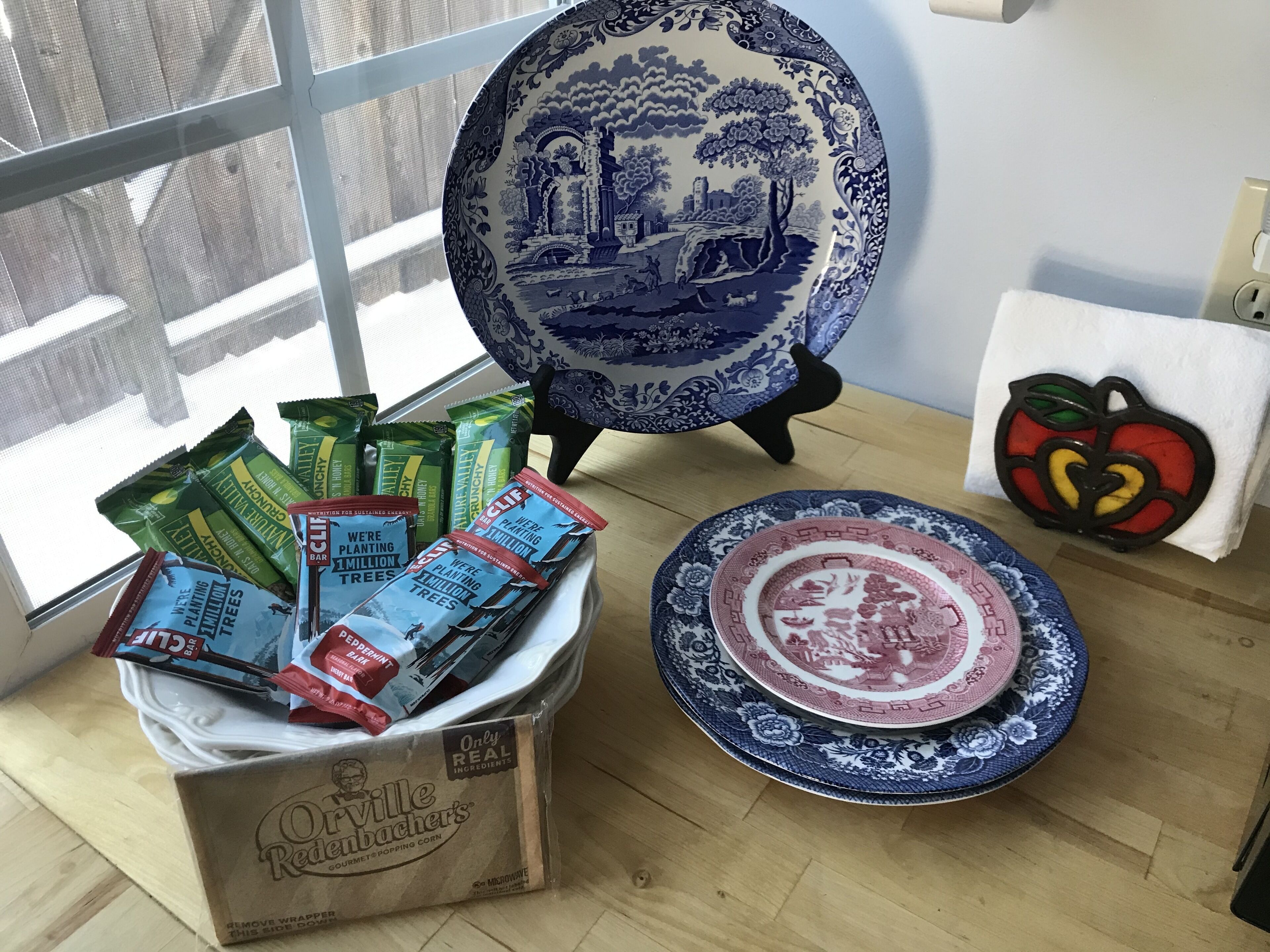 Una capsa de blat de moro torrat Gourmet Orville Redenbacher, un plat blau i blanc, i un objecte decoratiu amb forma de poma.