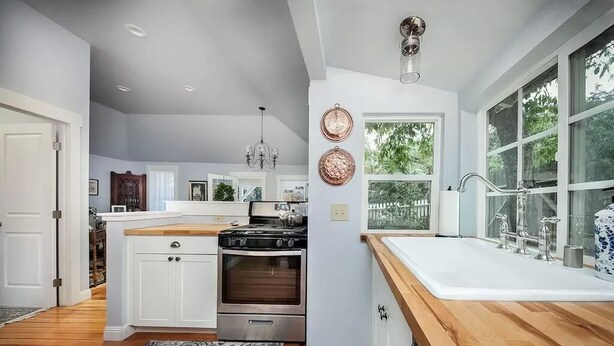Una cocina moderna con armarios blancos, encimera de madera, estufa de acero inoxidable y un amplio ventanal que proporciona luz natural.