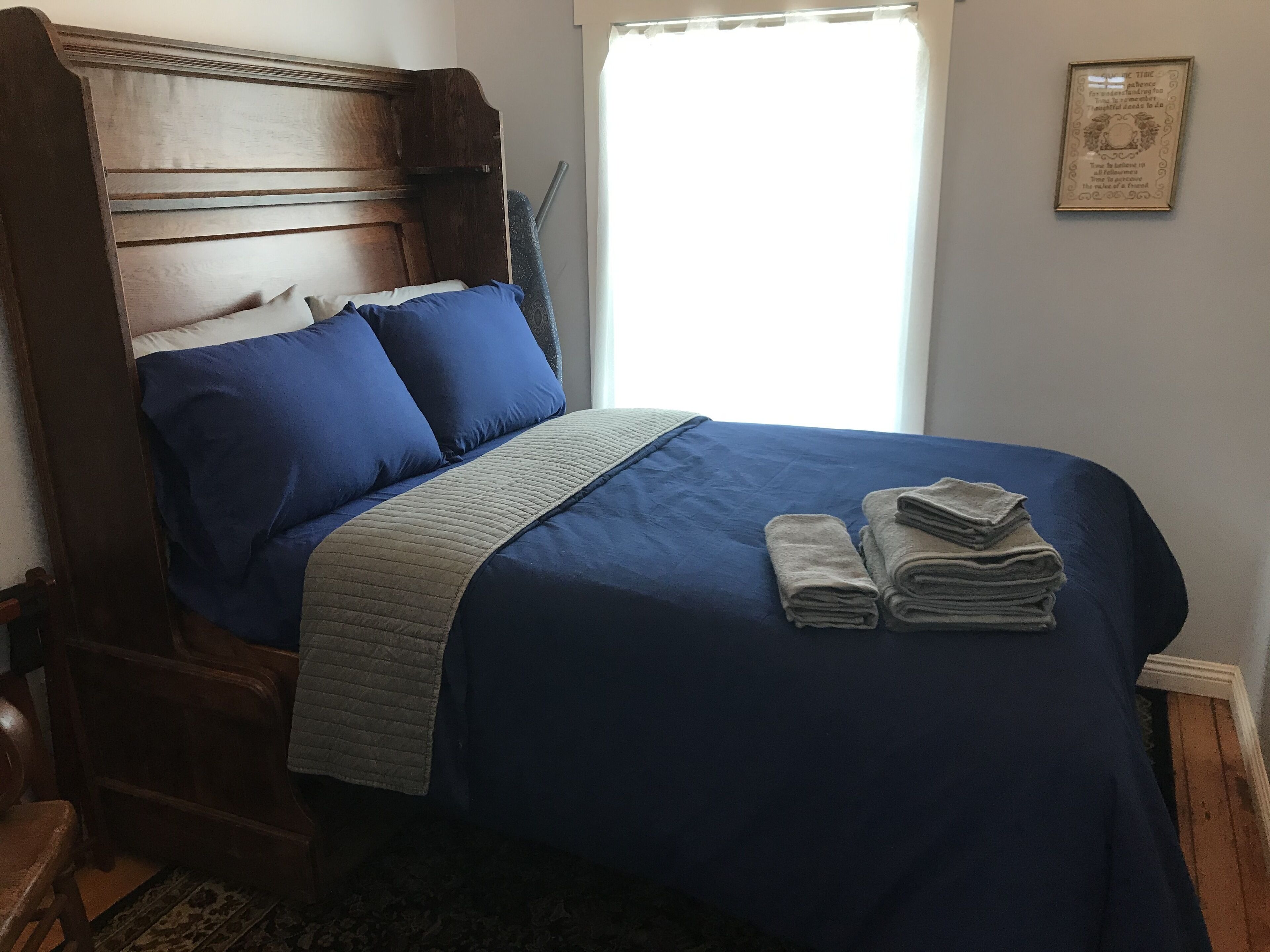 Un dormitorio con cabecera de madera, colcha azul y una pila de toallas sobre la cama.