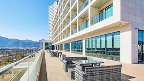 A rooftop terrace with outdoor seating, large windows, and a view of mountains. - Hotel Arina (Miryang)