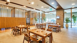 A modern restaurant with wooden tables and chairs, a decorative wall, and large windows allowing natural light. - Hotel Arina (Miryang)