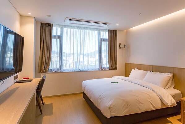 Habitación de hotel con cama, escritorio, silla, televisión y ventana con cortinas.