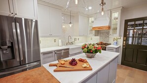 Moderni keittiö, jossa on ruostumattomasta teräksestä valmistetut kodinkoneet, keskellä oleva saareke, jossa on leikkuulauta, sekä koristeellinen maljakko.