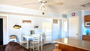 Una cocina compacta con armarios blancos, un refrigerador blanco y un comedor con mesa y sillas blancas.