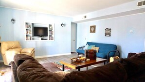 Una sala de estar con sofá, sillón y televisor sobre una estantería.
