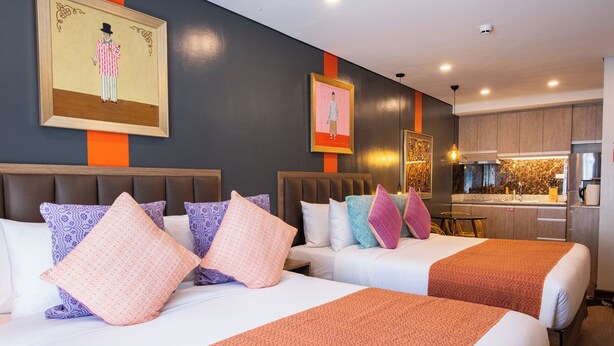 A hotel room with two beds, a kitchenette, and artwork on the walls. - UNWND Flats Makati (Makati)