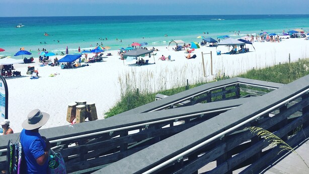 Een strand met een houten looppad, parasols en mensen die ontspannen.