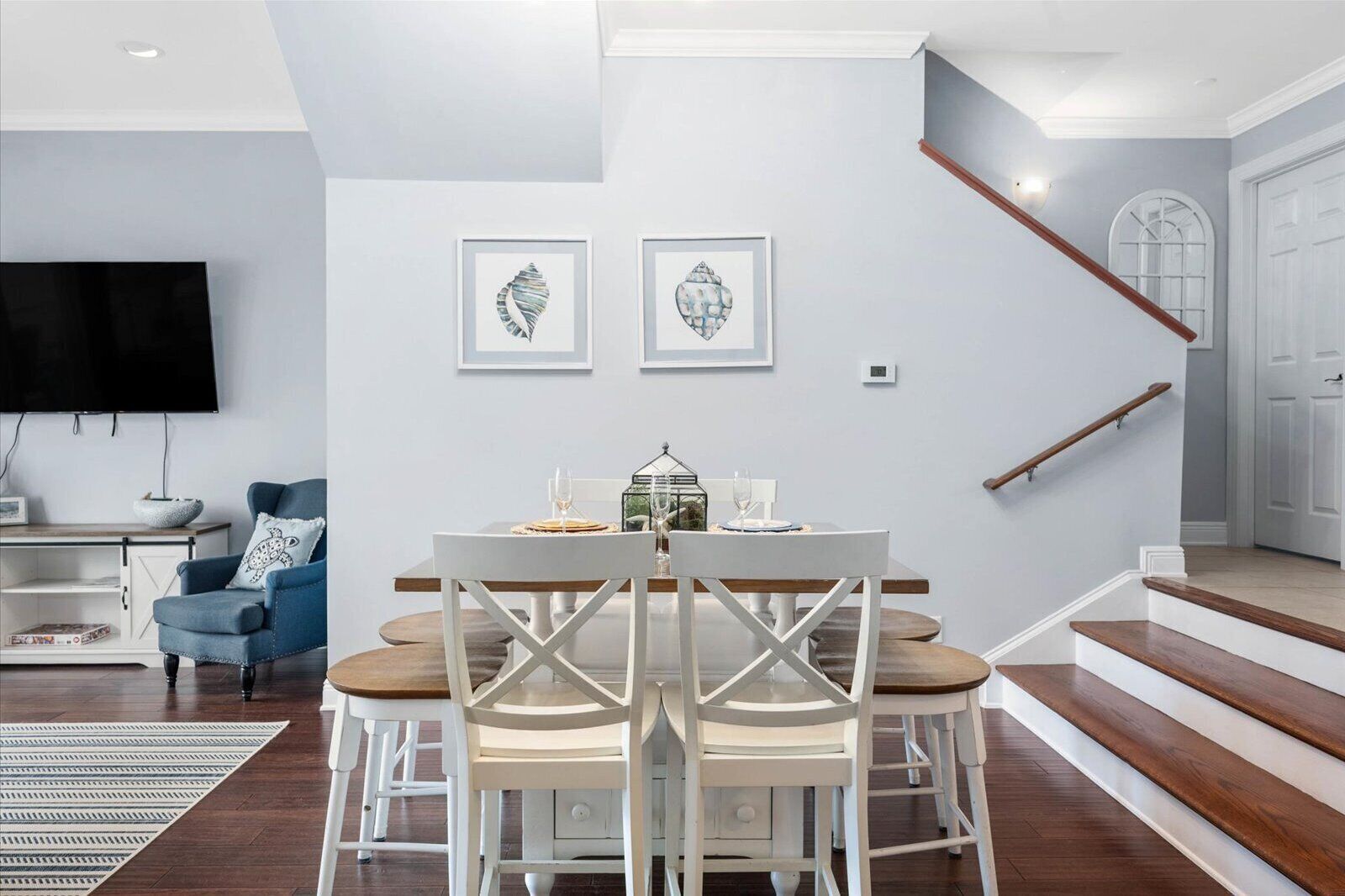 Un comedor con una mesa y sillas blancas, un sillón azul y un televisor de pantalla plana en la pared.