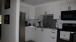 Una cocina moderna con armarios blancos, un refrigerador de acero inoxidable, un microondas y una estufa.