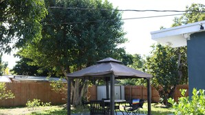 Un patio cubierto con una mesa y sillas, rodeado por una valla de madera y árboles.
