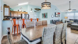 Zona pranzo con tavolo in legno e sedie in vimini, cucina con mobili in legno e lampadario, e soggiorno con divano e lampada.