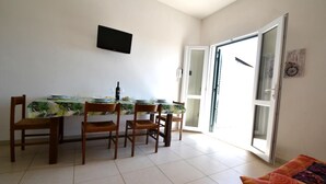 Un comedor con mesa, sillas, televisor montado en la pared y puerta corrediza de vidrio que da al exterior.