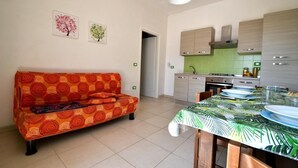 Un espacio habitable compacto con sofá, una mesa de comedor, kitchenette y dos cuadros colgados en la pared.