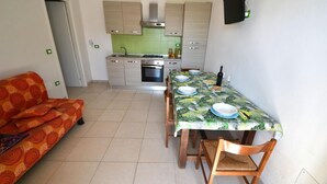 Una cocina compacta con una mesa de comedor preparada para cuatro personas, un sofá y un televisor montado en la pared.